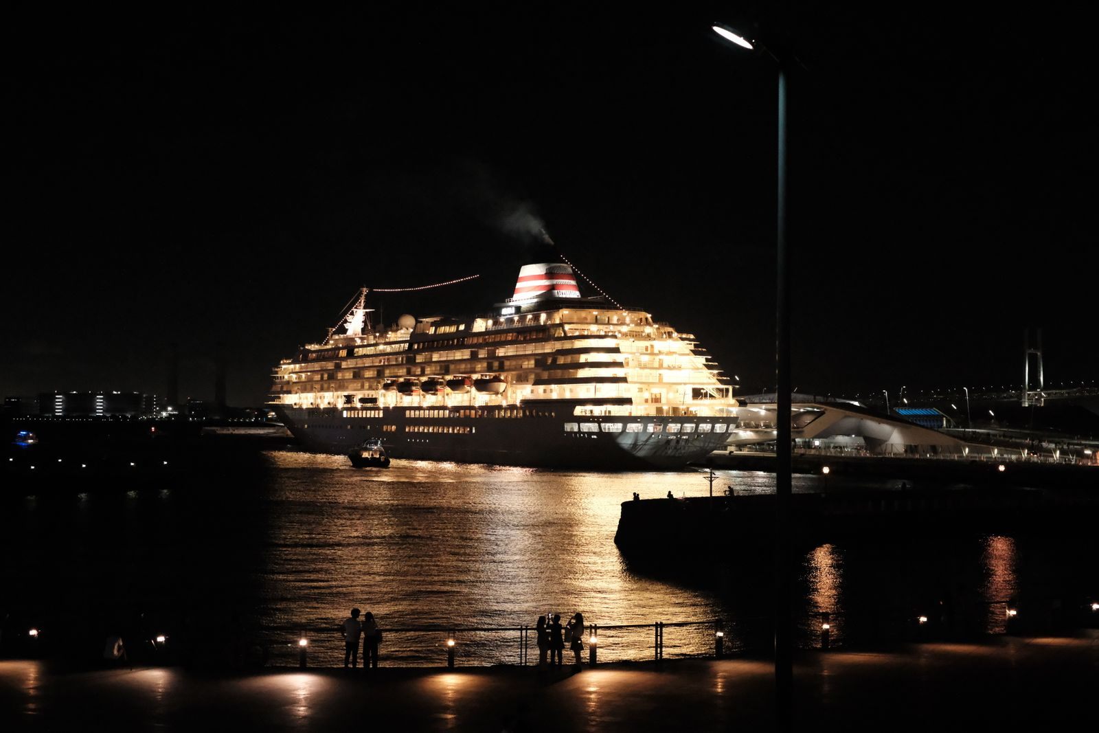 Cruise ship lit up at night beside a harbor promenade