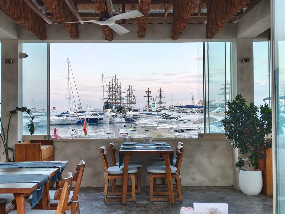 Restaurant tables by a large window overlooking a marina