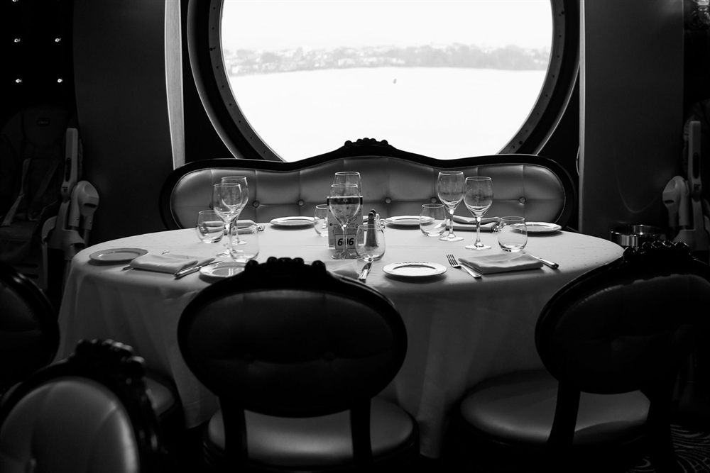 Formal ship dining room with round tables beneath a large porthole window