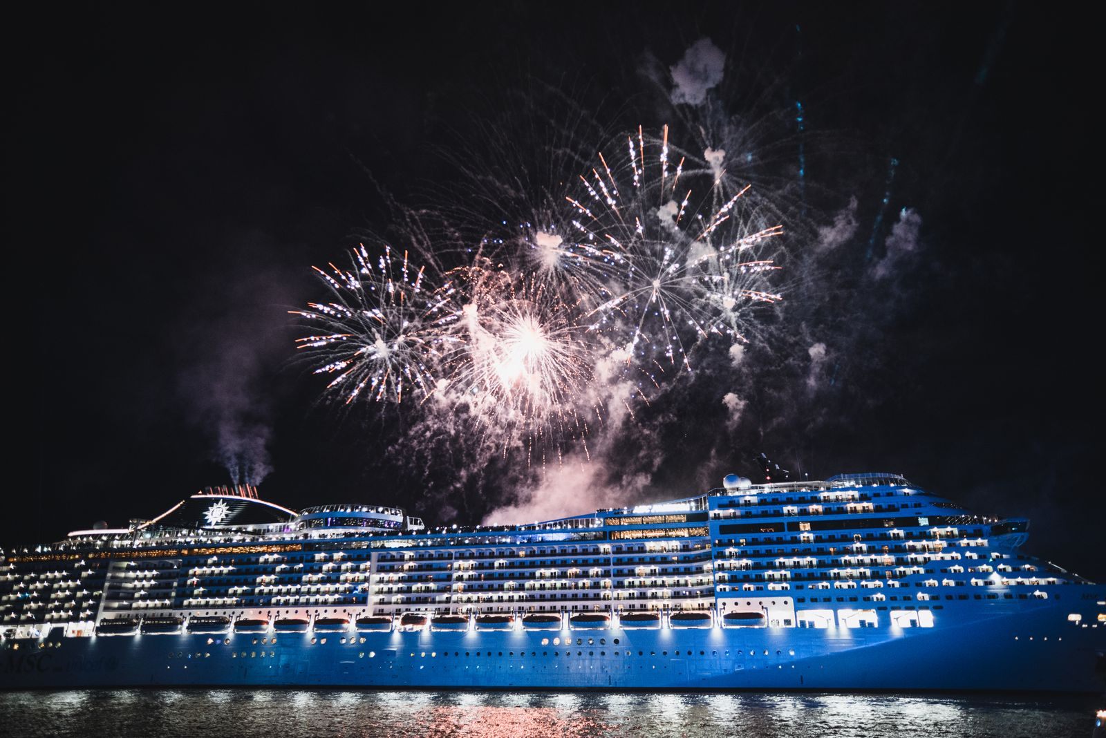 Fireworks bursting over a brightly lit cruise ship at night